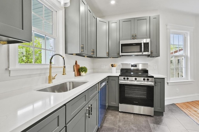 kitchen with stainless steel appliances, a sink, light countertops, gray cabinets, and baseboards