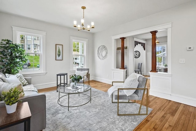 living area with decorative columns, wood finished floors, a chandelier, and baseboards