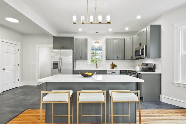 kitchen featuring stainless steel appliances, a kitchen breakfast bar, recessed lighting, baseboards, and gray cabinetry