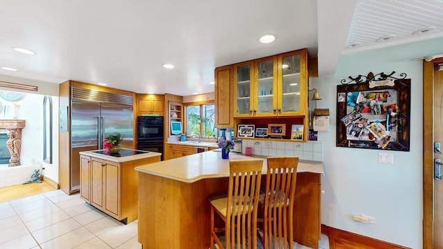 kitchen featuring black appliances, a center island, a peninsula, light countertops, and glass insert cabinets