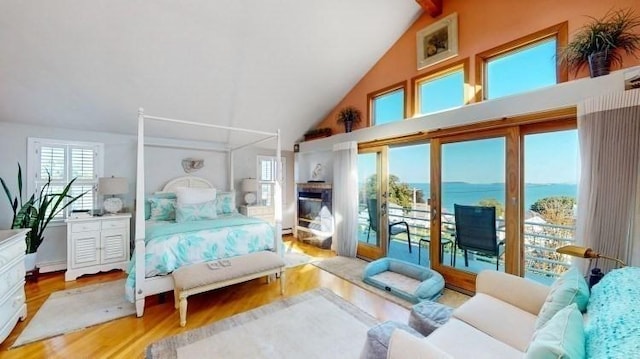 bedroom featuring a water view, high vaulted ceiling, a glass covered fireplace, wood finished floors, and access to exterior