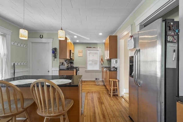 kitchen with appliances with stainless steel finishes, a breakfast bar, decorative light fixtures, ornamental molding, and light hardwood / wood-style flooring