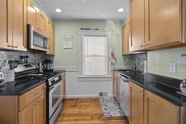 kitchen featuring sink, ornamental molding, appliances with stainless steel finishes, dark stone counters, and light hardwood / wood-style floors