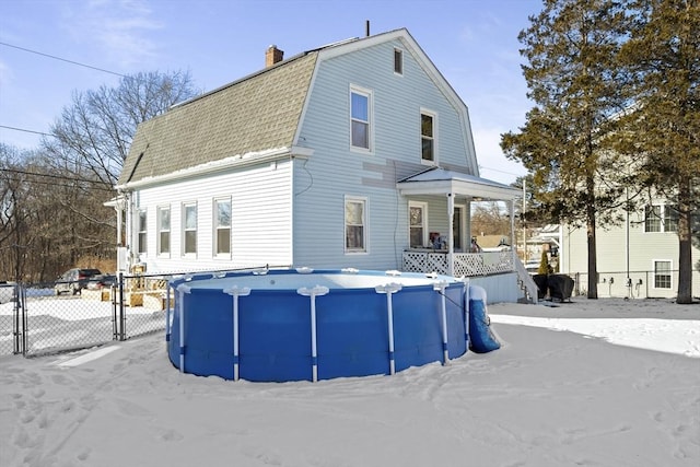 snow covered back of property featuring covered porch