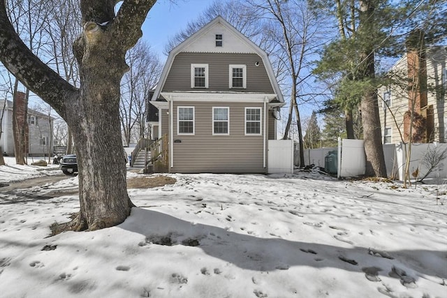 snow covered back of property with fence and a gambrel roof