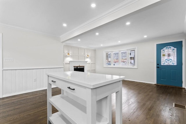 kitchen featuring crown molding, a brick fireplace, dark hardwood / wood-style flooring, a kitchen island, and white cabinets