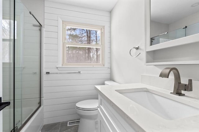 full bathroom featuring wooden walls, shower / bath combination with glass door, vanity, toilet, and tile patterned floors