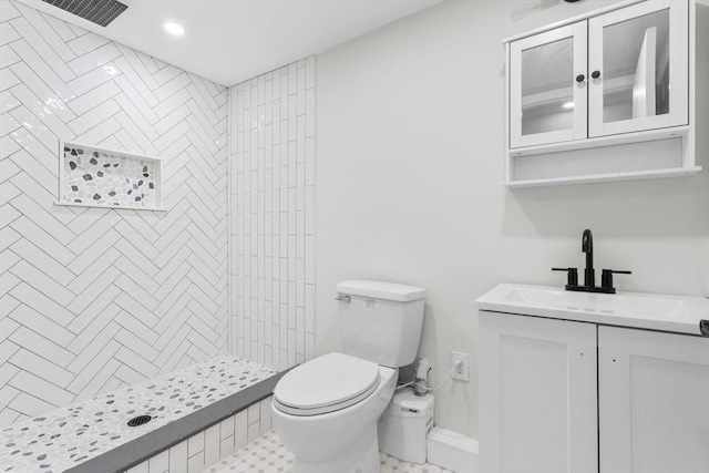 bathroom with a tile shower, vanity, and toilet