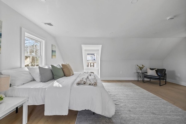 bedroom with vaulted ceiling, visible vents, baseboards, and wood finished floors