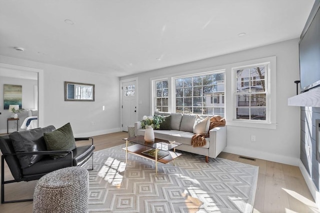 living room featuring visible vents, a fireplace, baseboards, and light wood-style floors