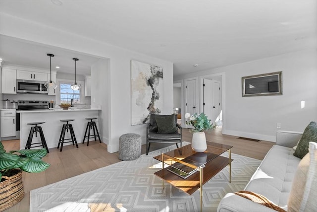 living area with visible vents, light wood-style flooring, and baseboards