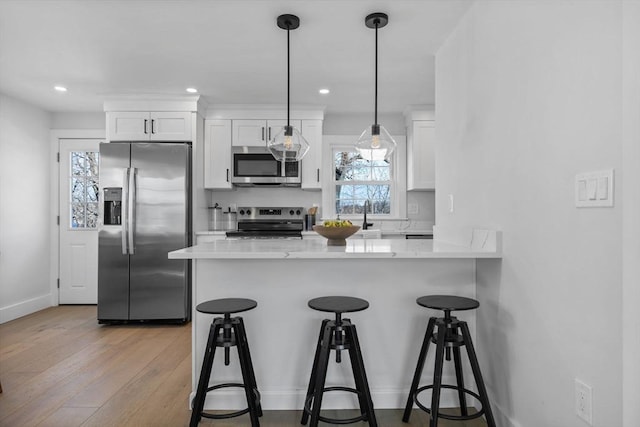 kitchen featuring a breakfast bar area, light wood finished floors, a peninsula, white cabinets, and appliances with stainless steel finishes