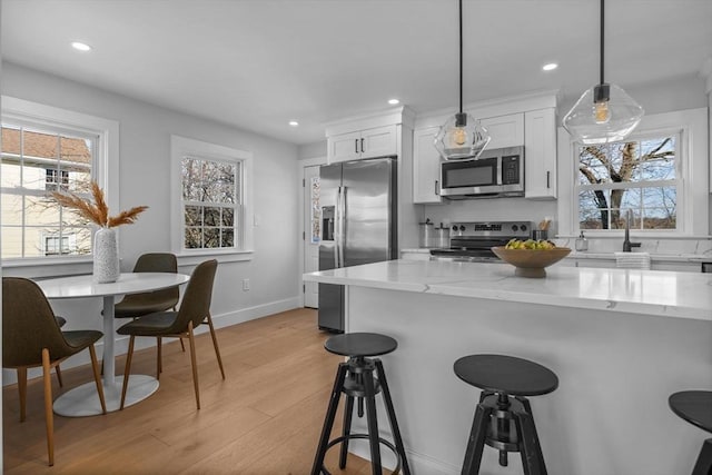 kitchen featuring a breakfast bar, a sink, white cabinetry, light wood-style floors, and appliances with stainless steel finishes