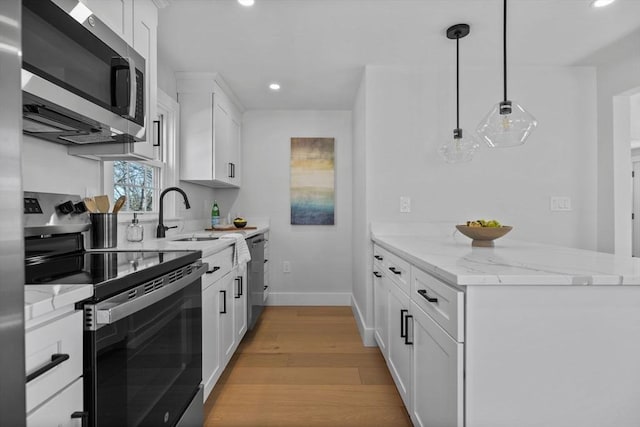 kitchen with light wood-style flooring, a sink, light stone counters, stainless steel appliances, and white cabinets