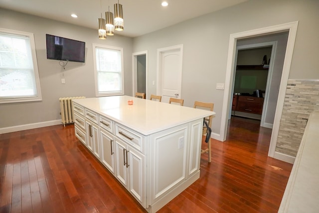 kitchen with hanging light fixtures, a breakfast bar, a kitchen island, dark hardwood / wood-style flooring, and radiator