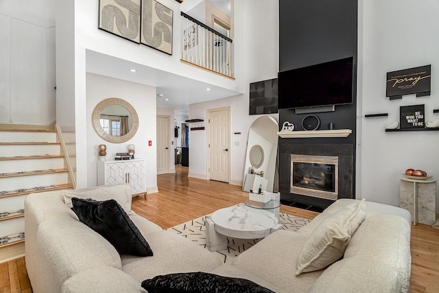 living area featuring a glass covered fireplace, stairs, a high ceiling, and wood finished floors