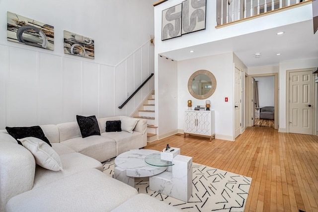 living room with stairs, recessed lighting, light wood-style flooring, a high ceiling, and a decorative wall