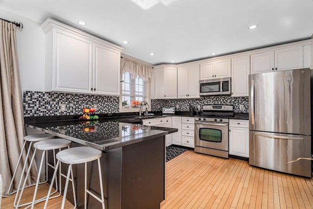 kitchen with light wood-type flooring, dark countertops, appliances with stainless steel finishes, a peninsula, and white cabinets