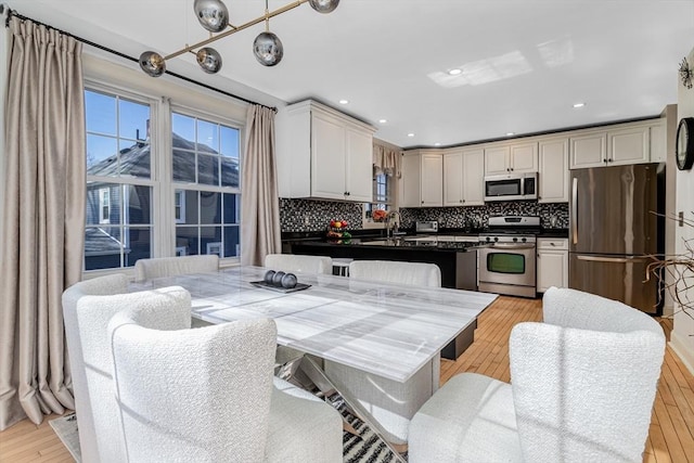 kitchen featuring a sink, stainless steel appliances, light wood-style floors, dark countertops, and backsplash