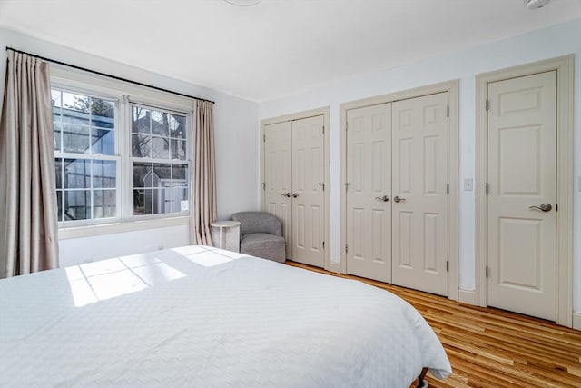 bedroom with two closets, light wood-type flooring, and baseboards