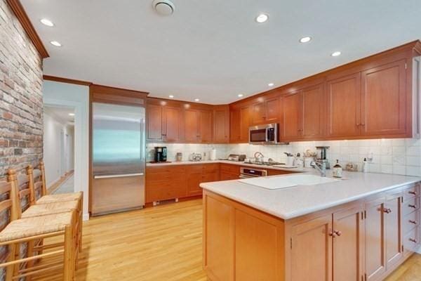 kitchen with a peninsula, light countertops, appliances with stainless steel finishes, light wood finished floors, and tasteful backsplash