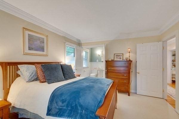 bedroom with light carpet, ensuite bath, and crown molding