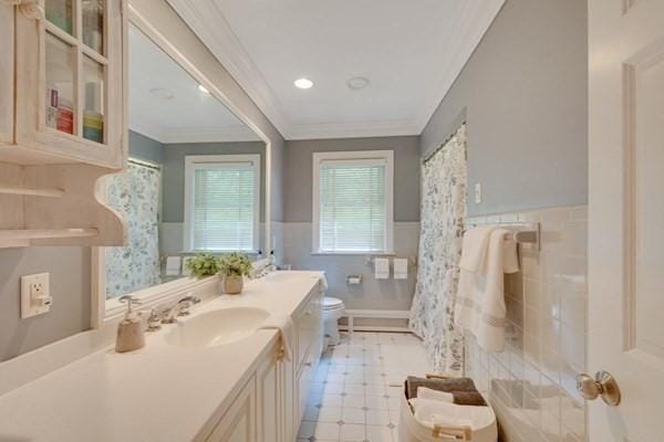 full bath with crown molding, double vanity, toilet, wainscoting, and a sink