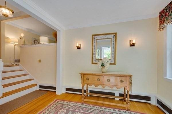 interior space with ornamental molding, a baseboard heating unit, stairway, and wood finished floors