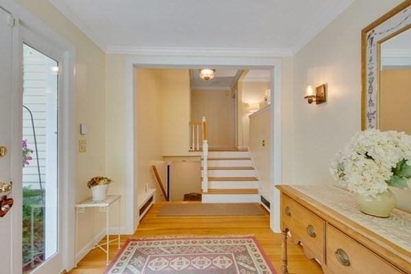 hall featuring light wood-type flooring, a baseboard heating unit, stairway, and ornamental molding