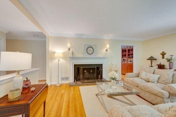 living area featuring ornamental molding, light wood-type flooring, a fireplace, and visible vents