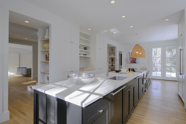 kitchen featuring built in shelves, sink, decorative light fixtures, a kitchen island with sink, and light hardwood / wood-style floors