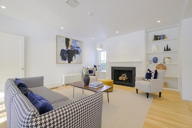 living room featuring built in features, radiator heating unit, light hardwood / wood-style floors, and a brick fireplace