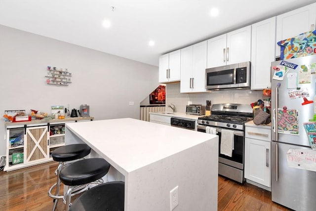 kitchen with dark wood-type flooring, backsplash, a kitchen island, appliances with stainless steel finishes, and light countertops