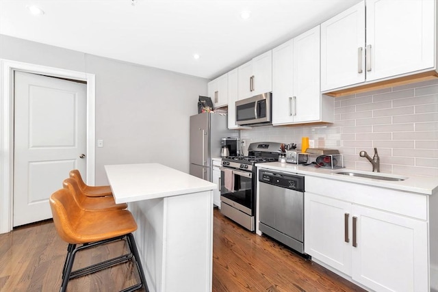 kitchen featuring a sink, tasteful backsplash, a kitchen island, wood finished floors, and appliances with stainless steel finishes
