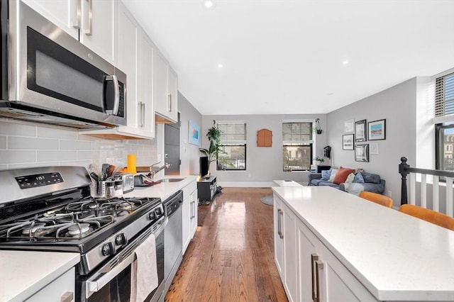 kitchen featuring backsplash, open floor plan, white cabinetry, appliances with stainless steel finishes, and light wood finished floors