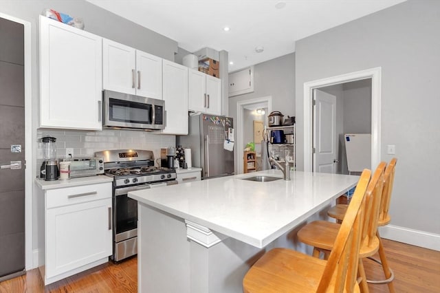 kitchen featuring decorative backsplash, appliances with stainless steel finishes, light wood-type flooring, and a sink