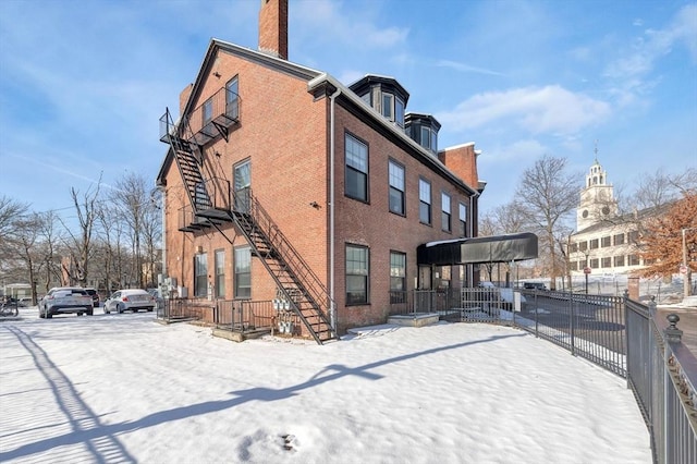 snow covered back of property with brick siding, stairway, a chimney, and fence