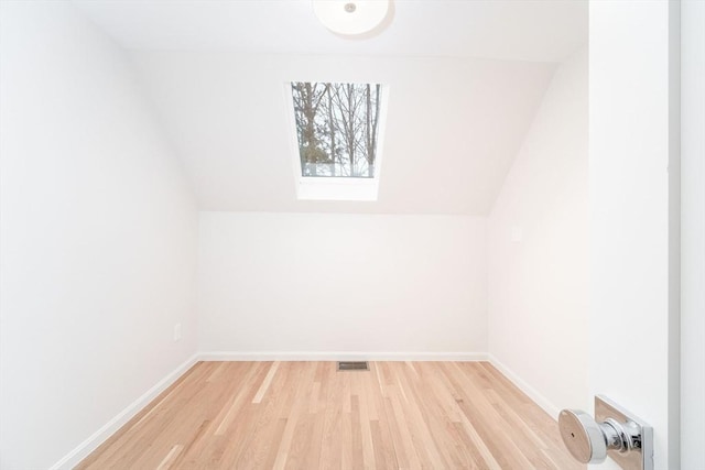 additional living space featuring light wood-type flooring, a skylight, baseboards, and vaulted ceiling