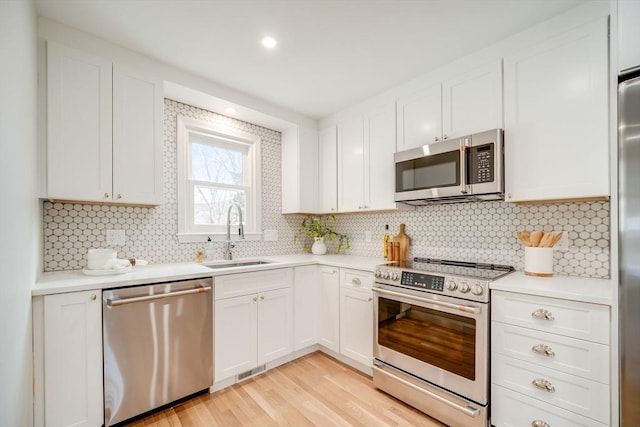 kitchen with appliances with stainless steel finishes, a sink, light wood finished floors, tasteful backsplash, and light countertops