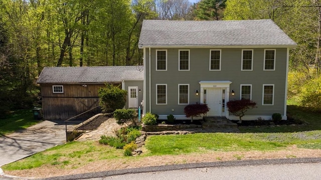 colonial house with concrete driveway, a front yard, and a shingled roof