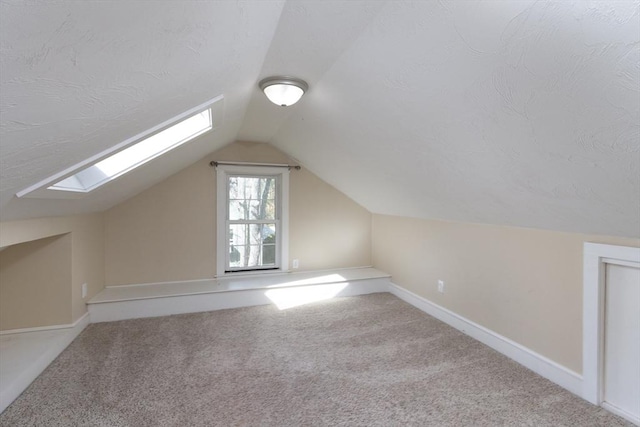 bonus room featuring a textured ceiling, carpet floors, baseboards, and vaulted ceiling with skylight