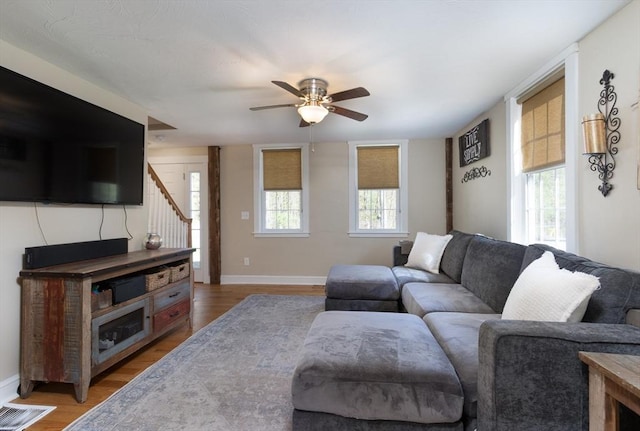 living area featuring light wood-style floors, baseboards, ceiling fan, and stairs