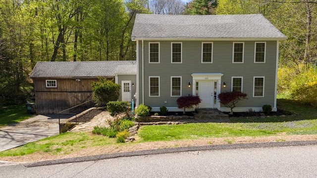 colonial inspired home featuring concrete driveway, a shingled roof, and a front lawn