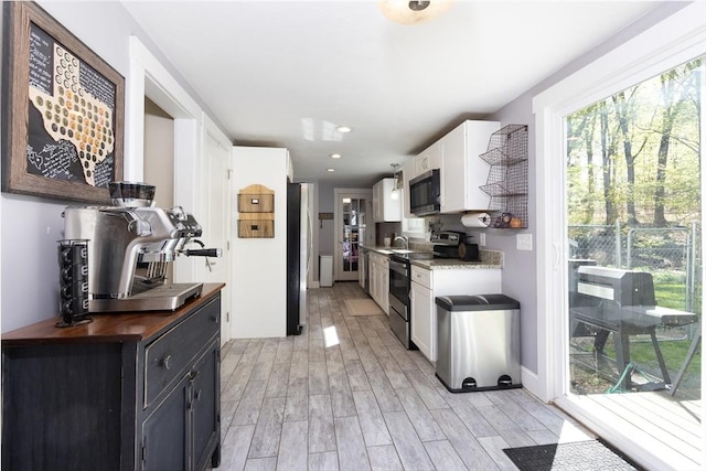 kitchen with baseboards, a sink, stainless steel appliances, white cabinets, and light wood-type flooring