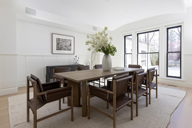 dining room featuring light wood-style flooring, a wainscoted wall, visible vents, lofted ceiling, and a decorative wall