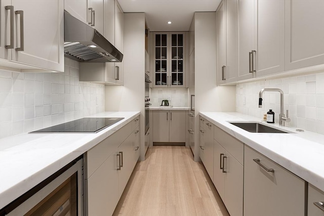 kitchen featuring light wood-type flooring, black electric cooktop, under cabinet range hood, wine cooler, and a sink
