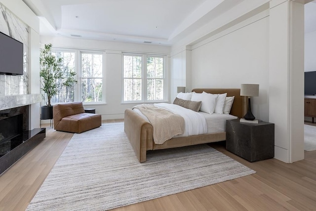 bedroom featuring a tray ceiling, light wood-type flooring, and multiple windows