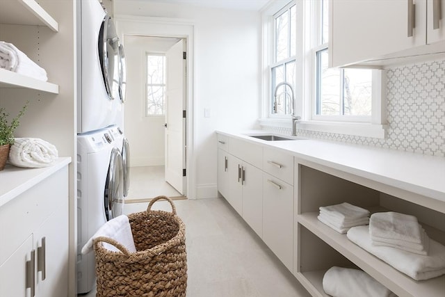 clothes washing area featuring baseboards, stacked washer / drying machine, a sink, and cabinet space