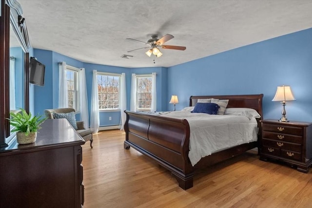 bedroom with a baseboard heating unit, a ceiling fan, visible vents, and light wood-type flooring