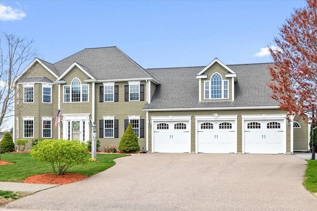 colonial house with a garage, a front lawn, roof with shingles, and aphalt driveway